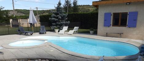 A swimming pool with two hot tubs, surrounded by lounge chairs and a pebble bed.