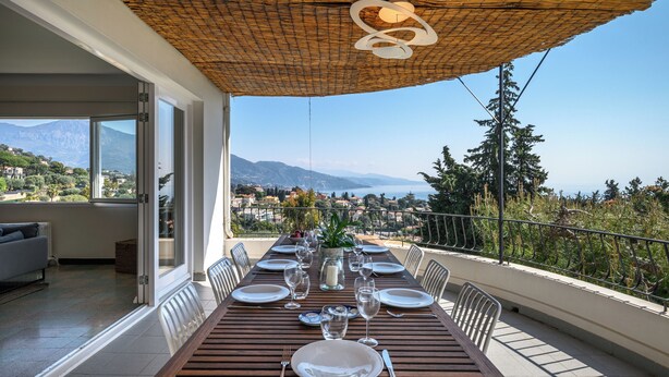 Mesa de comedor para seis personas en un balc ón con vistas a montañas y un pueblo.