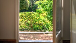 Una puerta abierta que da a un jardín con diversas plantas y un camino de ladrillo.
