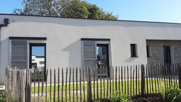 A modern building with a grey facade, a wooden fence, and a grassy yard.