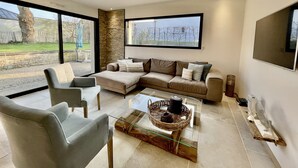 En moderne stue med et glasbord, en beige sofa og en grå lænestol.