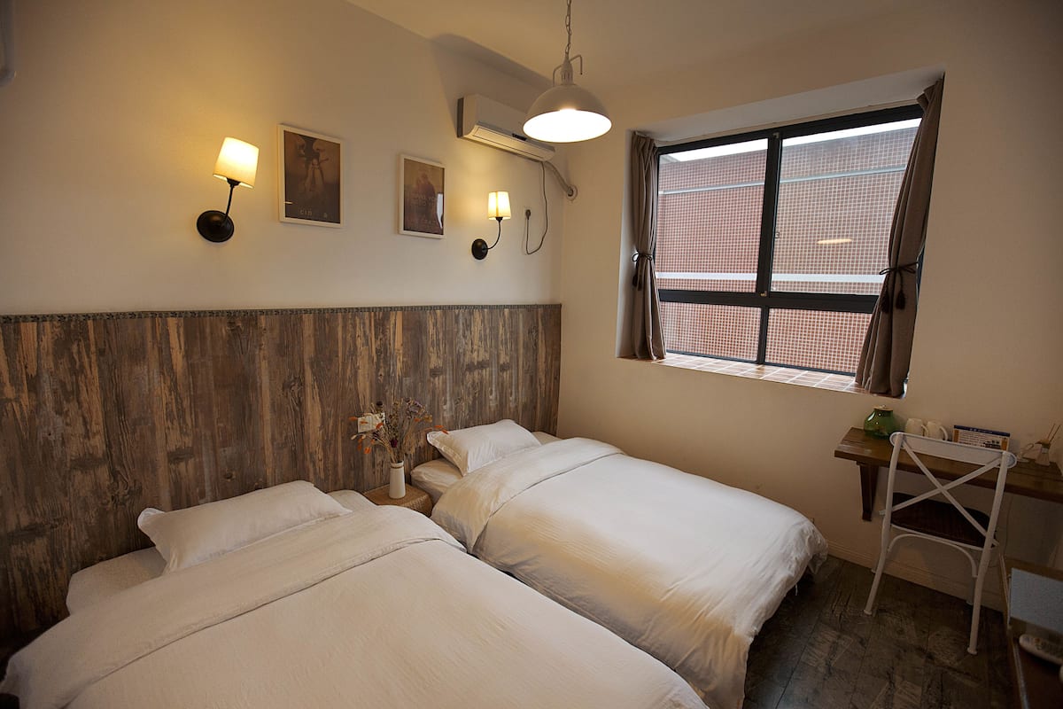 A bedroom with two beds, a wooden headboard, a window with a view, and a desk with a chair.