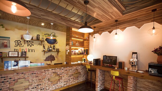 A cozy bar area with a brick wall, wooden ceiling, and hanging lights. There are stools, a counter with a coffee machine, and shelves with bottles and decorations. - Zhangjiajie MINI Inn (Zhangjiajie)
