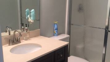 A bathroom with a sink, mirror, toilet, and shower.