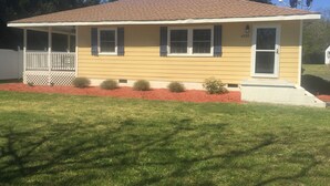 A single-story house with a front porch, a small front yard with red mulch, and a clear blue sky.
