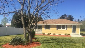 A single-story house with a yellow exterior, a red roof, and a white fence.
