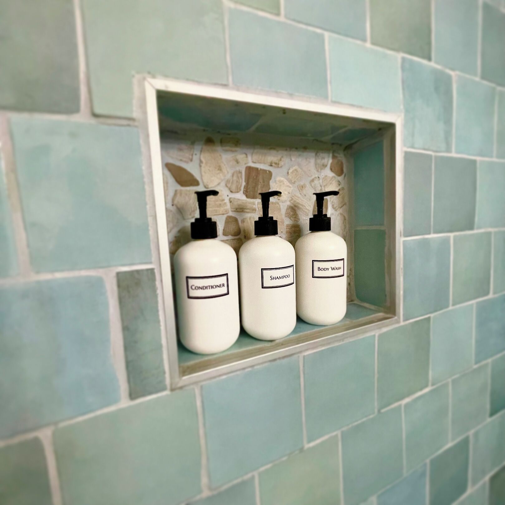 A bathroom shelf with three bottles labeled conditioner, shampoo, and body wash.