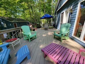 A wooden deck with Adirondack chairs, a picnic table, and a blue umbrella.
