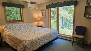 A bedroom with a bed, a chair, a nightstand with a lamp, and a window with a view of trees. - Your Lakeside Paradise: A/C, Private Dock, Kayaks & Rowboat on Dexter Pond! (Wayne)