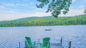A lake with a dock, two green chairs, and a boat. - Your Lakeside Paradise: A/C, Private Dock, Kayaks & Rowboat on Dexter Pond! (Wayne)