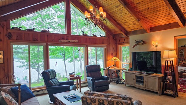 A cabin interior with large windows, a television, and a fireplace. - Your Lakeside Paradise: A/C, Private Dock, Kayaks & Rowboat on Dexter Pond! (Wayne)