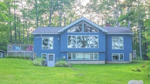 A two-story house with a large front window, a deck, and a grassy yard. - Your Lakeside Paradise: A/C, Private Dock, Kayaks & Rowboat on Dexter Pond! (Wayne)