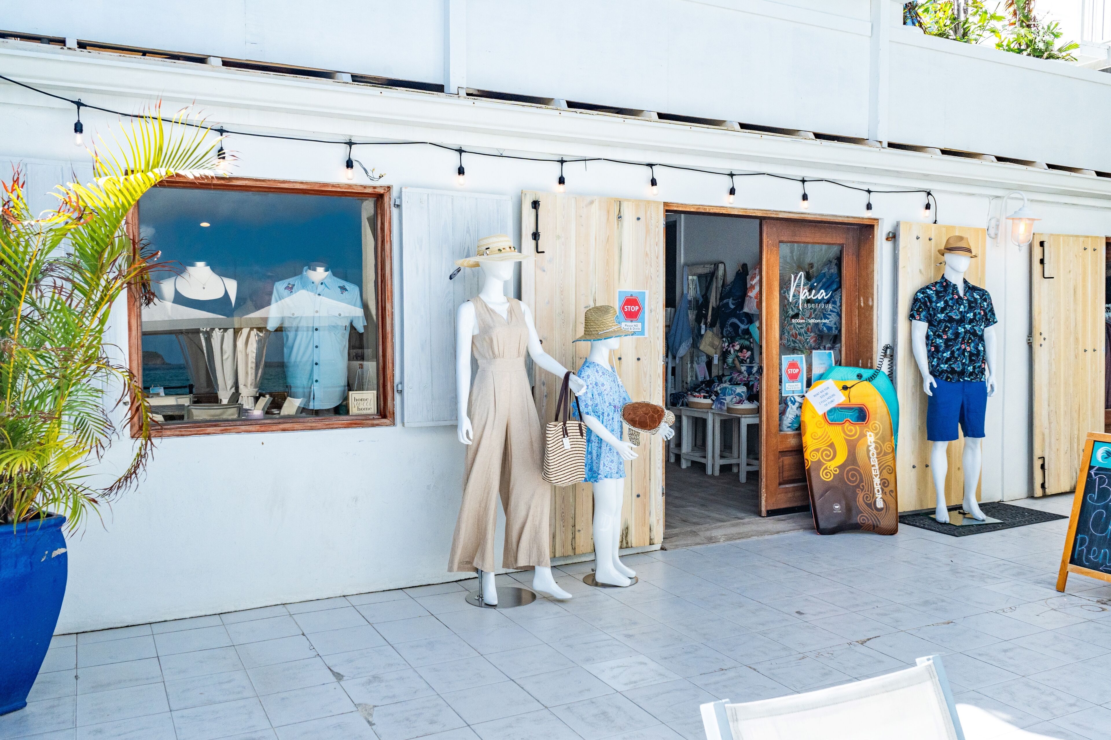 Un escaparate con maniquíes exhibiendo ropa veraniega informal, una puerta de madera y un cartel.
