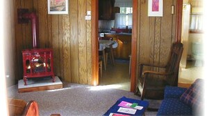 Uma sala de estar aconchegante com uma lareira a lenha vermelha, um sofá azul e uma área de jantar visível através de uma porta aberta.