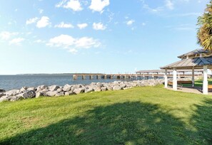 A coastal view with a pier extending into the water, a grassy area with a gazebo, and a rocky shoreline.