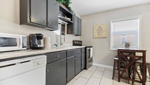 A kitchen with dark cabinets, a microwave, a coffee maker, and a window with blinds. - Beach Cottage -optional BIKES - Walk 2 Shops & Fun (Saint Simons Island)