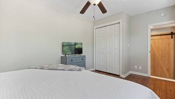 Une chambre à coucher avec un lit, un ventilateur de plafond, une télévision, une armoire et une porte.