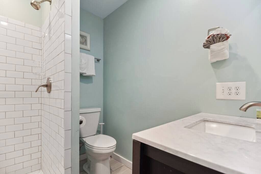 Un baño con paredes de azulejos blancos, un inodoro blanco, un lavamanos con encimera de mármol y un perchero con una toalla.