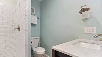 Un baño con paredes de azulejos blancos, un inodoro blanco, un lavamanos con encimera de mármol y un perchero con una toalla.