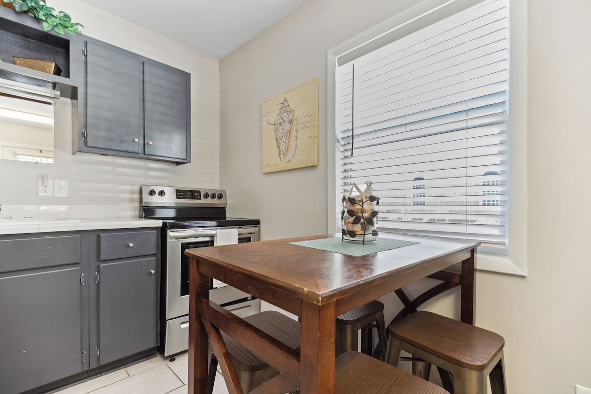A kitchen with grey cabinets, a wooden table, and a window with blinds.