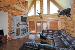 A log cabin interior with a stone fireplace, leather sofa, and a mounted deer head. - Galilee Lodge CUSTOM BUILT LOG CABIN NEAR BEACH & WALK TO THE DOWNTOWN, W/VIEW (Garden City)