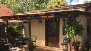 Uma casa térrea com varanda coberta, pérgola de madeira e um pequeno espaço de estar ao ar livre com mesa e cadeiras.