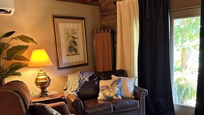 Uma sala de estar aconchegante com um sofá de couro marrom, um tapete estampado, teto de madeira e uma janela grande com cortinas.