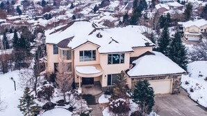 A large, two-story house with a snow-covered roof and driveway, surrounded by a suburban neighborhood.