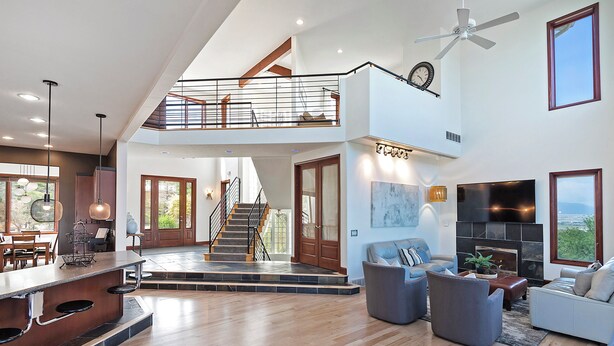 A spacious living area with a high ceiling, a staircase leading to an upper level, a fireplace, and a large window offering a view.