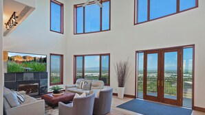 A spacious living room with a fireplace, comfortable seating, large windows, and a balcony with a view.