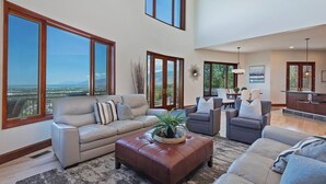 A spacious living room with large windows, a leather sofa, a coffee table, and a dining area with a view.