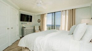 Quarto com uma cama grande, ventoinha no teto, cômoda, televisão e vista para o oceano.