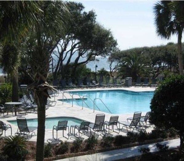 Relax by the serene pool surrounded by lush greenery and shaded by trees.