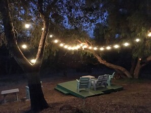 Ein Sitzbereich im Freien mit Tisch und Stühlen unter einem Baum, geschmückt mit Lichterketten.