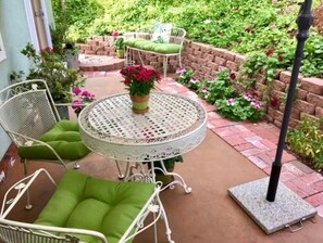 Relax in the serene patio area with a round table and comfortable seating, surrounded by lush greenery and a vibrant potted plant.