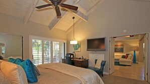 A bedroom with a large bed, a desk, a chair, a ceiling fan, and a TV.
