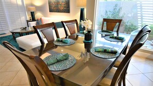 A dining area with a glass-top table, wooden chairs, and green placemats.