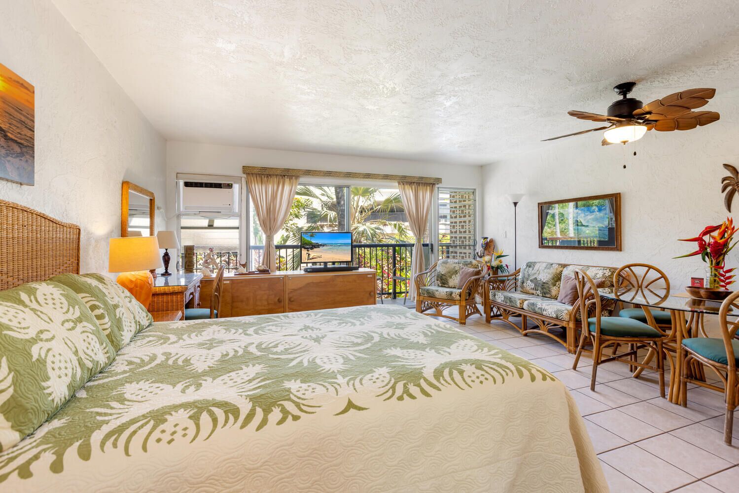 A room with a bed, a TV, a balcony, wicker furniture, and a ceiling fan.