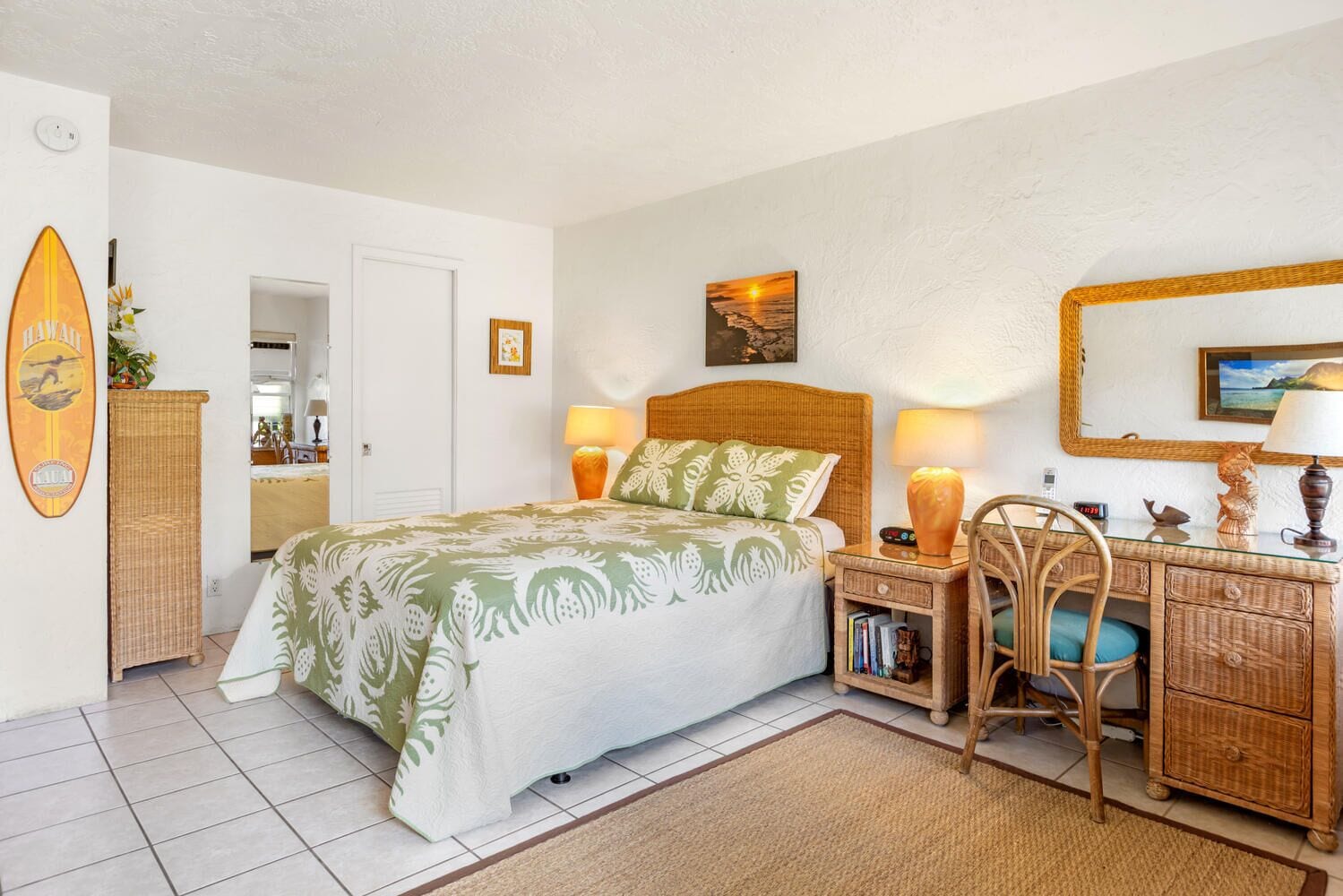A bedroom with a bed, bedside tables, a desk, wicker furniture, and a beach-themed wall decoration.