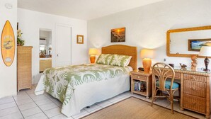 Ein Schlafzimmer mit einem Bett, Nachttischen, einem Schreibtisch, Korbmöbeln und einer Wanddekoration im Strandstil.