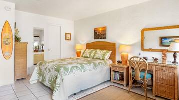A bedroom with a bed, bedside tables, a desk, wicker furniture, and a beach-themed wall decoration.
