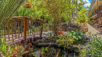 A garden with a small pond, a wooden bridge, and various plants and flowers.