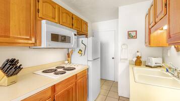 A kitchen with wooden cabinets, a white stove, a microwave, a refrigerator, and a sink.