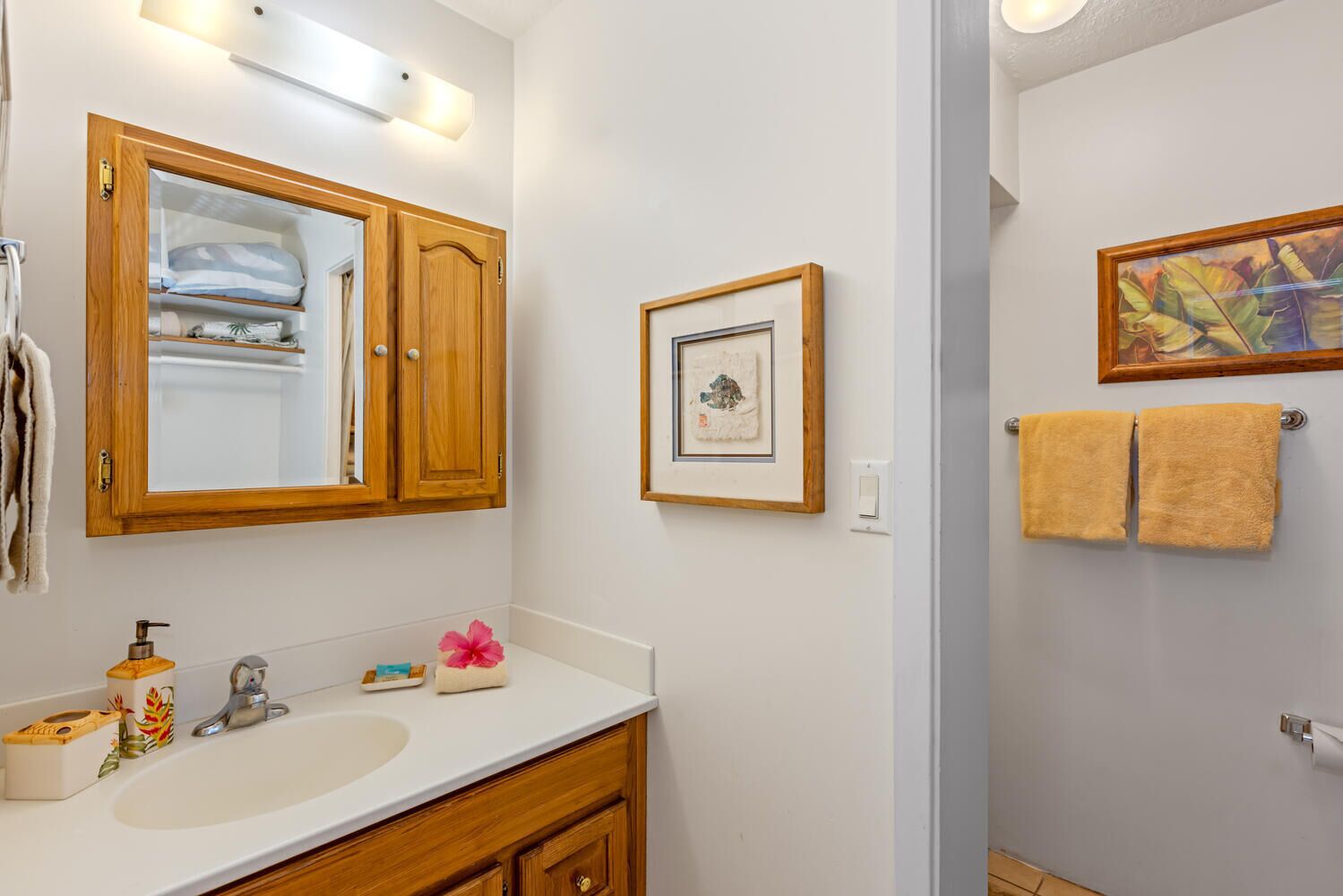 A bathroom with a wooden vanity, a white sink, a mirror, and a framed picture on the wall.