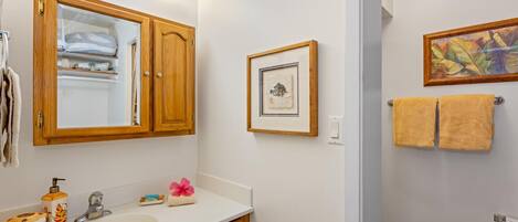 A bathroom with a wooden vanity, a white sink, a mirror, and a framed picture on the wall.