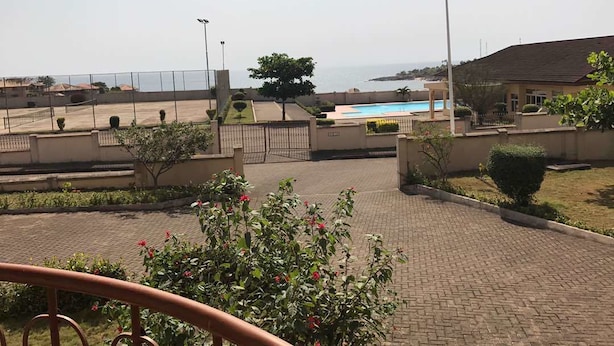 A view of a residential area with a swimming pool, a gate, and a clear view of the sea. - The Villa 9 at Seaview Estate (Freetown)