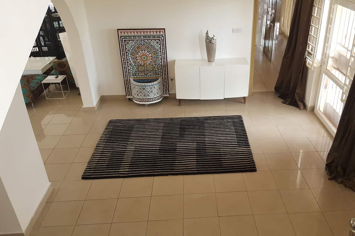 Un vaste espace de vie doté d’un sol carrelé, d’un tapis décoratif, d’une console blanche, d’un vase et d’une décoration murale à motifs.