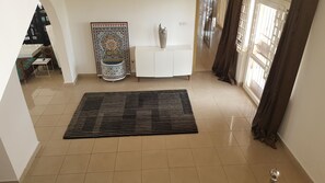 A spacious living area with a tiled floor, a decorative rug, a white console table, a vase, and a patterned wall hanging. - The Villa 9 at Seaview Estate (Freetown)