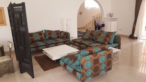 A living room with a sectional sofa, a coffee table, and a decorative black partition. - The Villa 9 at Seaview Estate (Freetown)