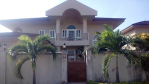 A two-story house with a gated entrance, a balcony, and palm trees. - The Villa 9 at Seaview Estate (Freetown)